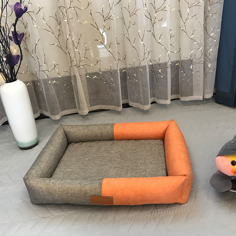 Gray and orange pet bed on a light gray floor with a decorative curtain in the background.