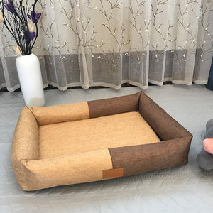Brown and beige pet bed on a light wooden floor with a decorative curtain in the background.