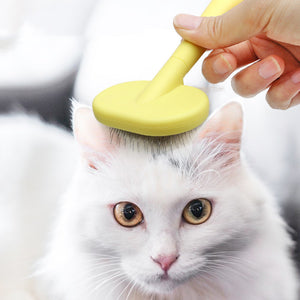White cat being brushed with a yellow brush by a hand