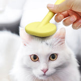 White cat being brushed with a yellow brush by a hand