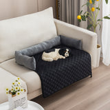 Dog lying on a black quilted pet bed on a beige couch with decorative pillows.