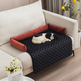 Dog lying on a black quilted pet bed with red pillows on a beige couch.