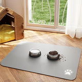 Gray pet mat with two bowls on a wooden floor near a window with green grass outside.