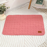 Pink textured bath mat on a white textured surface with a plant and books in the background.